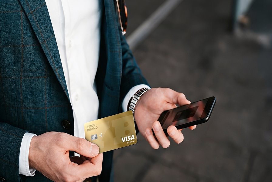 A man in a suit holds a gold Visa card and a phone with the Wallester app in his hand.